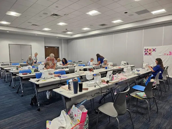 Blanketeers working at sewing machines around tables